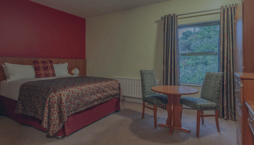 Cozy bedroom with bed, red accent wall, window, and small table with two chairs