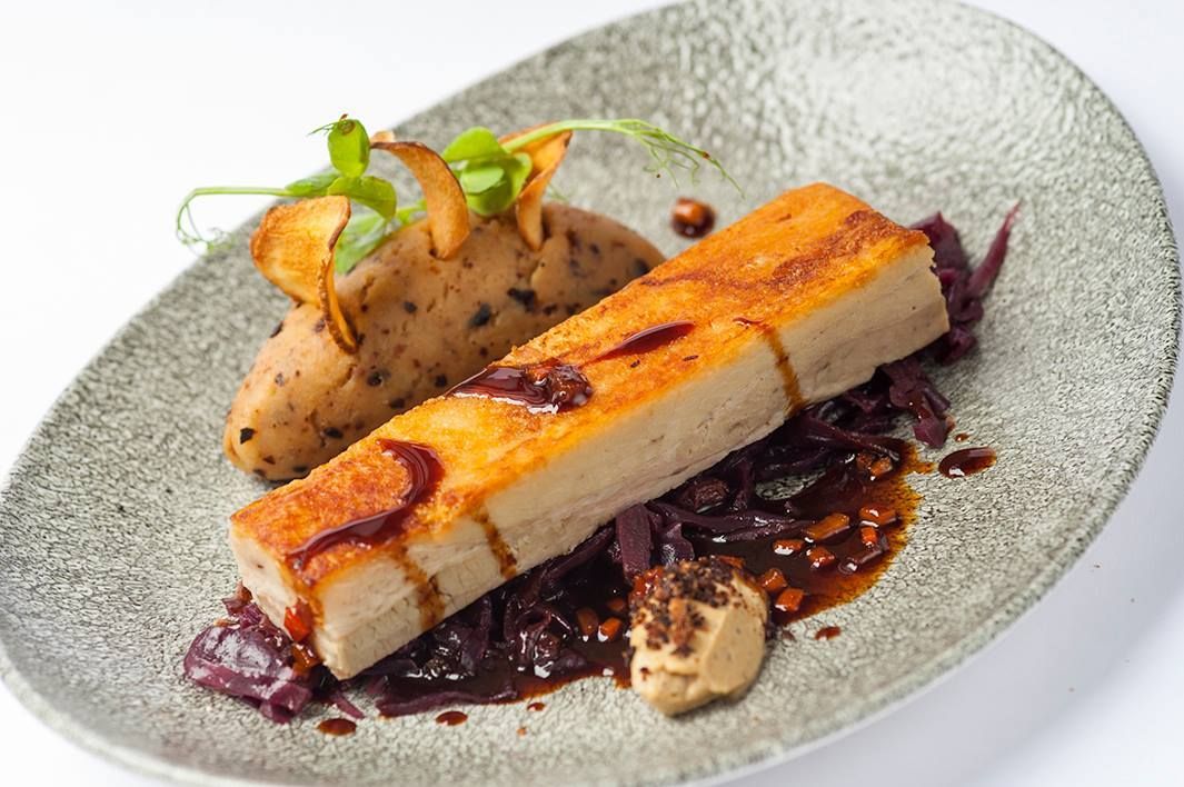 Plated gourmet dish with seared fish, sauce, and vegetables on a gray plate