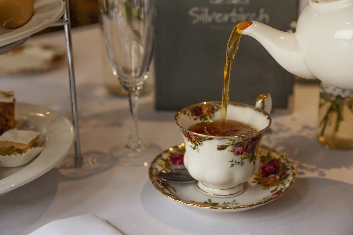 Tea being poured into a floral teacup on a saucer at a table setting