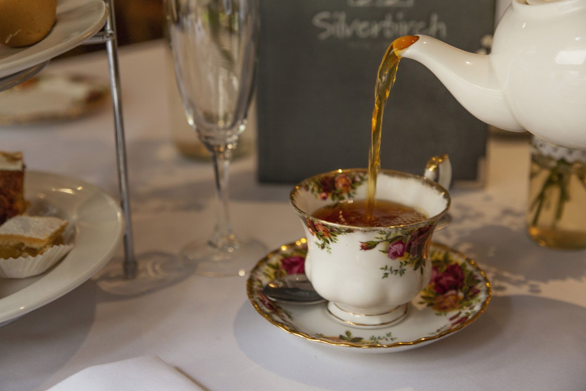 Tea being poured into a floral porcelain cup and saucer at a formal table setting