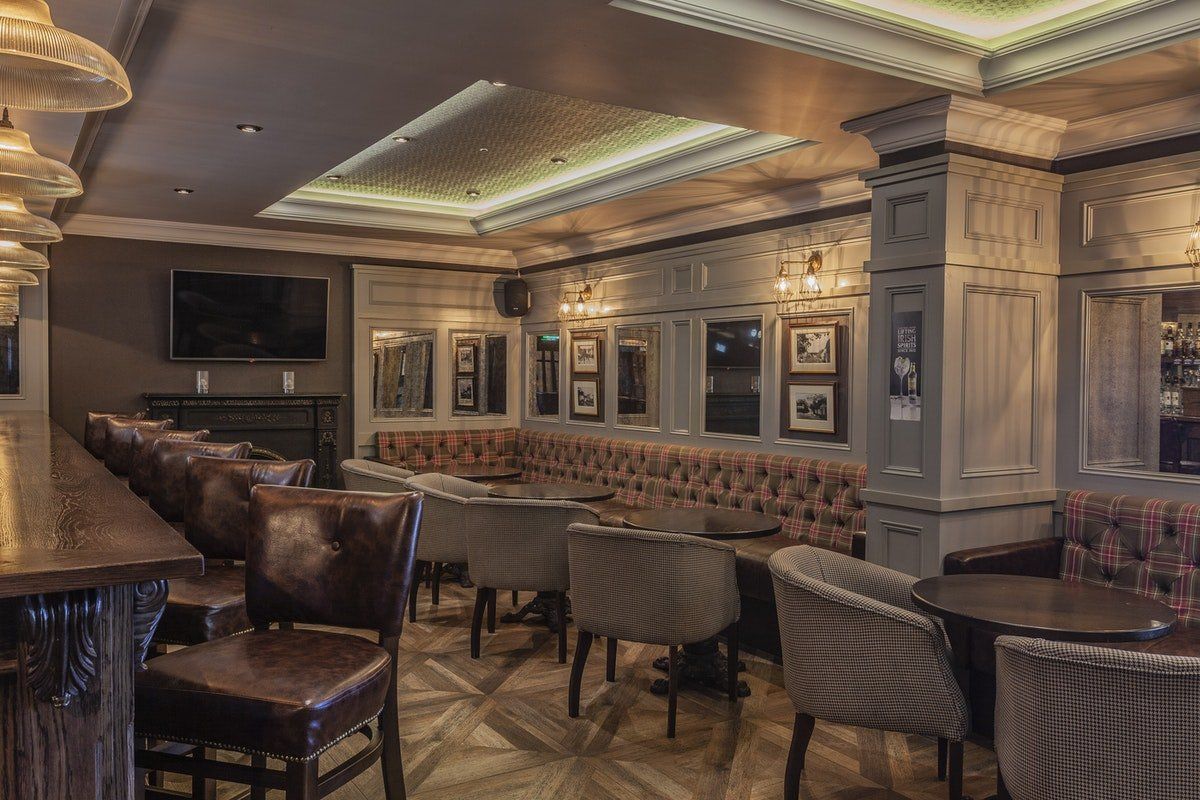 Elegant dimly lit lounge with tufted booths, bar stools, wall art, and ornate ceiling lighting