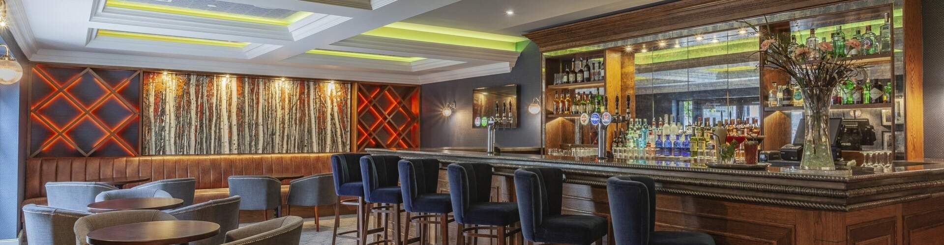 Modern upscale bar interior with booths, stools, warm wood accents, and colorful ceiling lighting