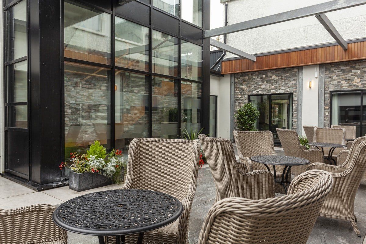 Patio seating area with wicker chairs and tables beside a modern glass building
