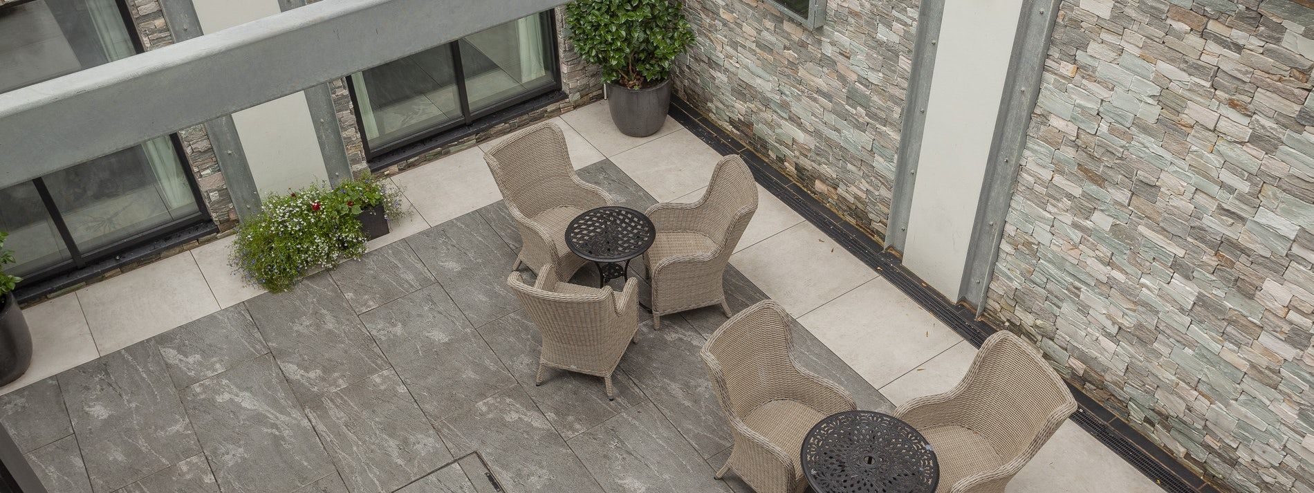 Outdoor patio with wicker chairs around a small table beside a stone wall and glass railing.
