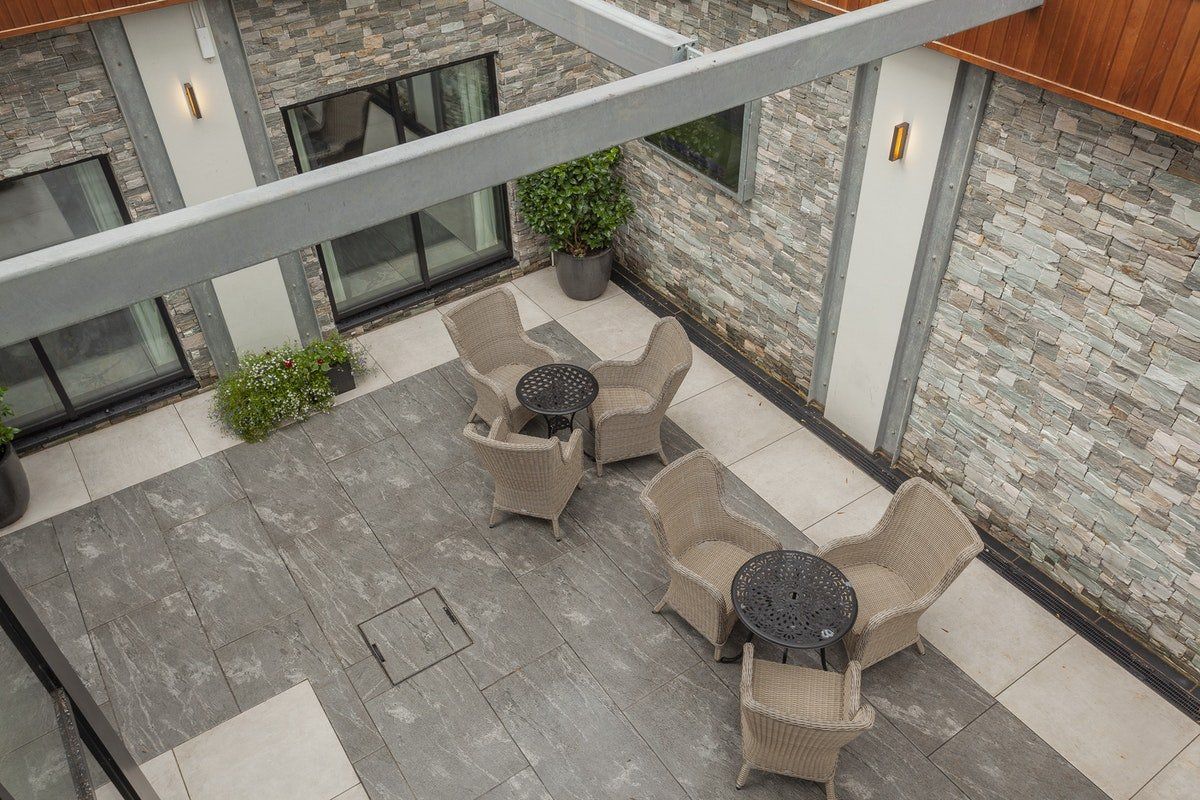 Courtyard patio with beige chairs around two tables, stone walls, and a gray tiled floor