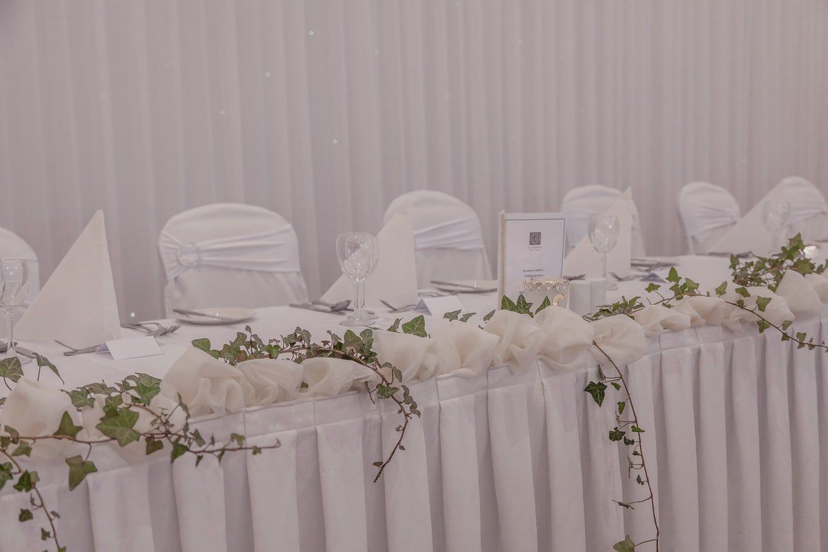 White banquet table set with white chair covers and floral greenery garlands in a softly lit reception hall