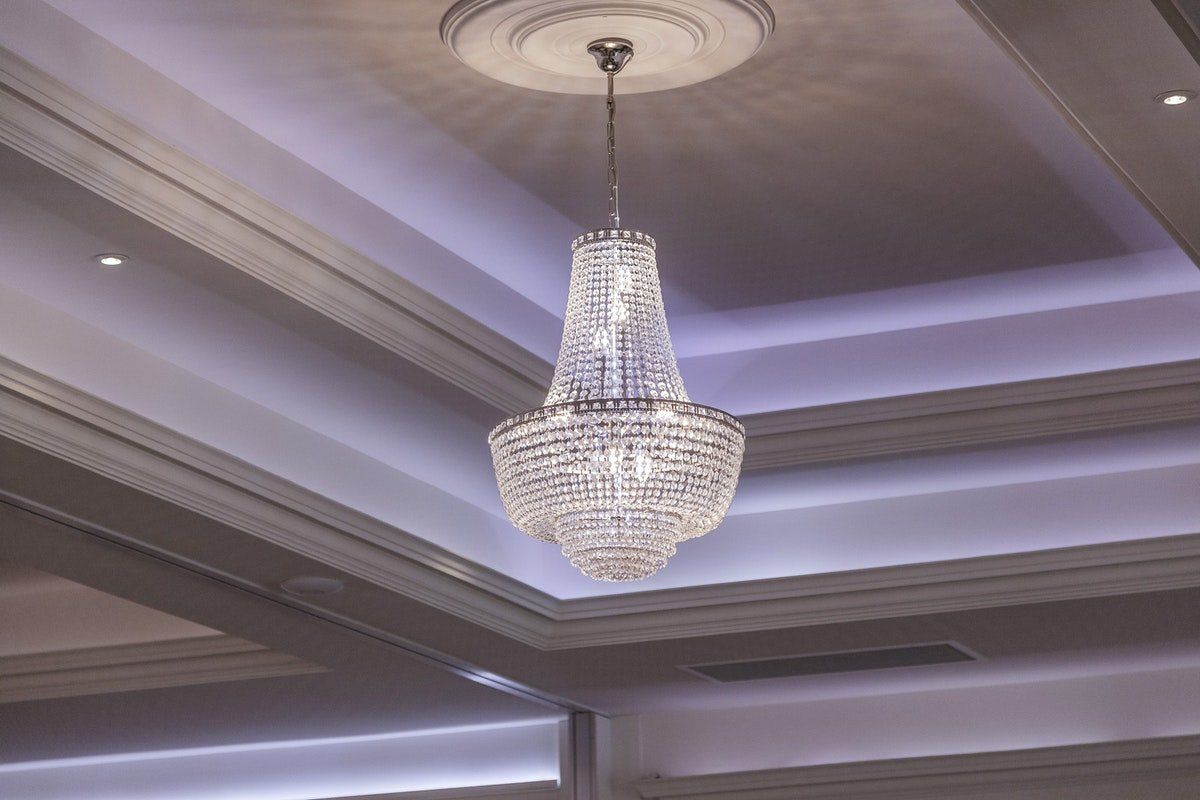 Crystal chandelier hanging from a coffered ceiling with soft purple accent lighting.