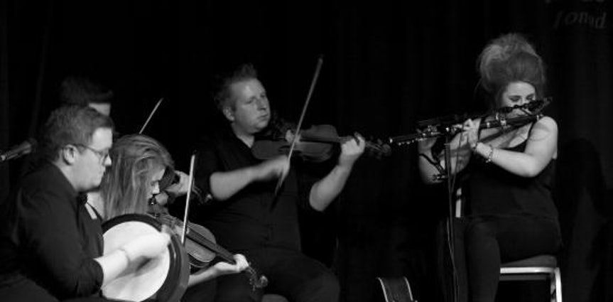 Four musicians playing string instruments on a dark stage, focused on their performance