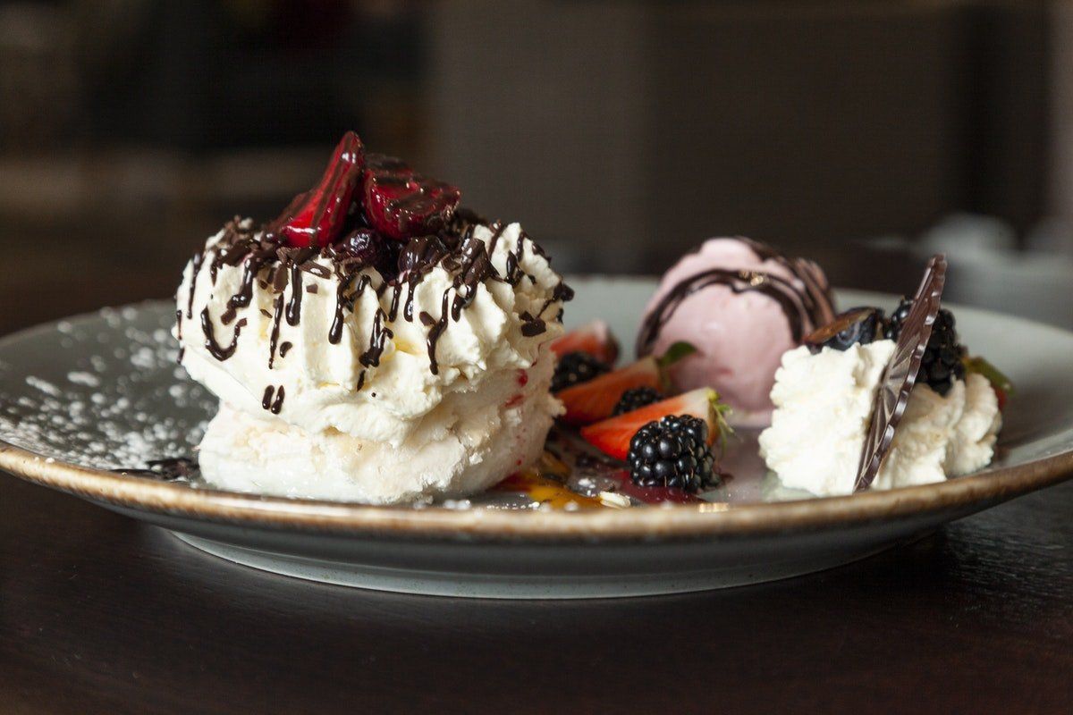 Dessert plate with whipped cream, chocolate drizzle, berries, and a scoop of ice cream on a dark table