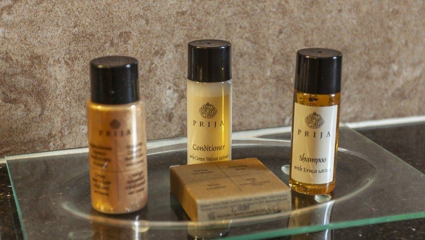Three small cosmetic bottles and a soap bar on a glass shelf against a beige wall.