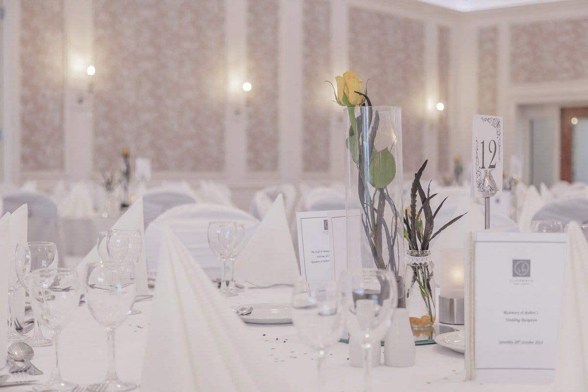 Elegant banquet hall tables set with white linens, candles, and floral centerpieces in a soft, bright room