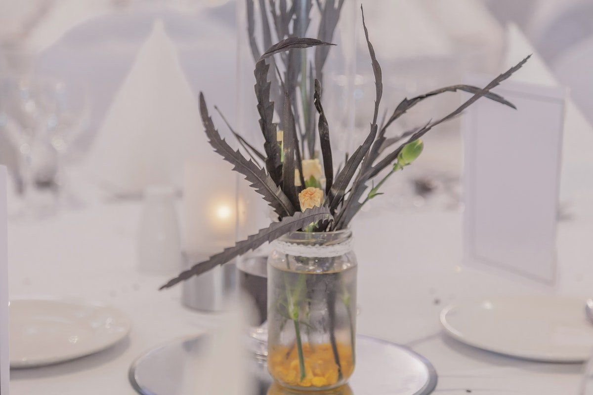 Glass vase centerpiece with dark feathers and yellow accents on a white table setting