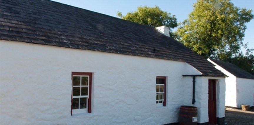 White cottage with dark roof, two small windows, and a red door in sunny daylight