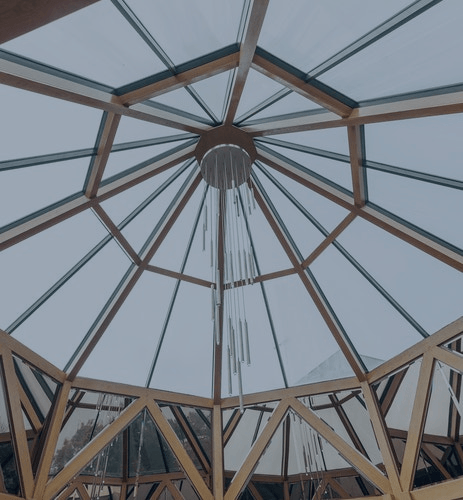 Glass-roofed wooden pavilion ceiling with radial beams and a central skylight, viewed upward