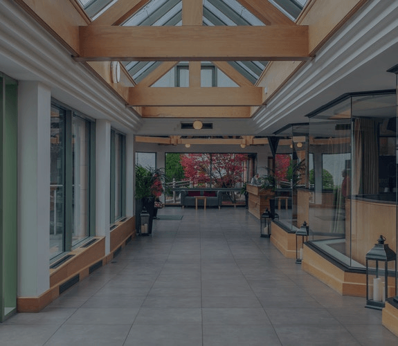 Modern indoor walkway with glass walls, wood beams, and potted plants in a bright atrium