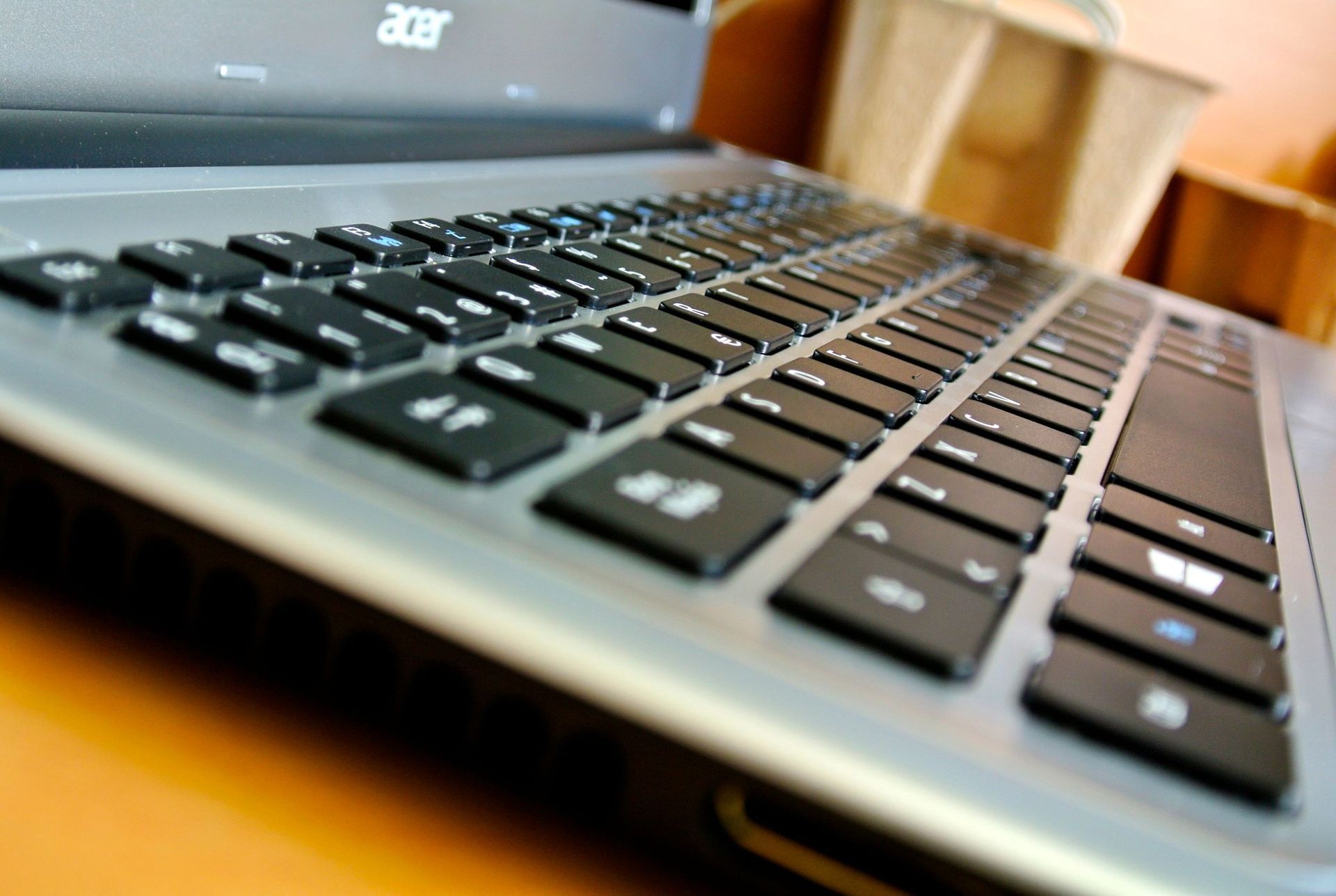 Close-up of a black laptop keyboard on a wooden desk, angled view with Acer logo visible