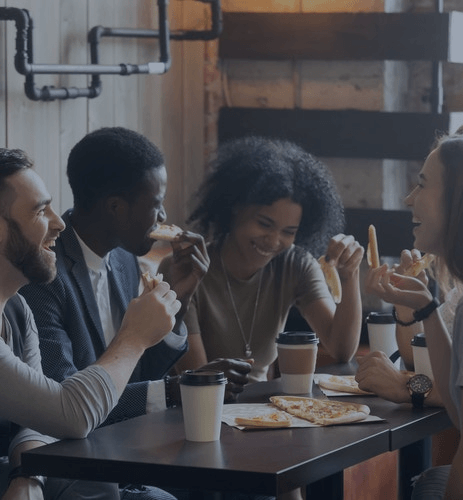 Friends chatting over coffee and pizza at a table in a cozy café.