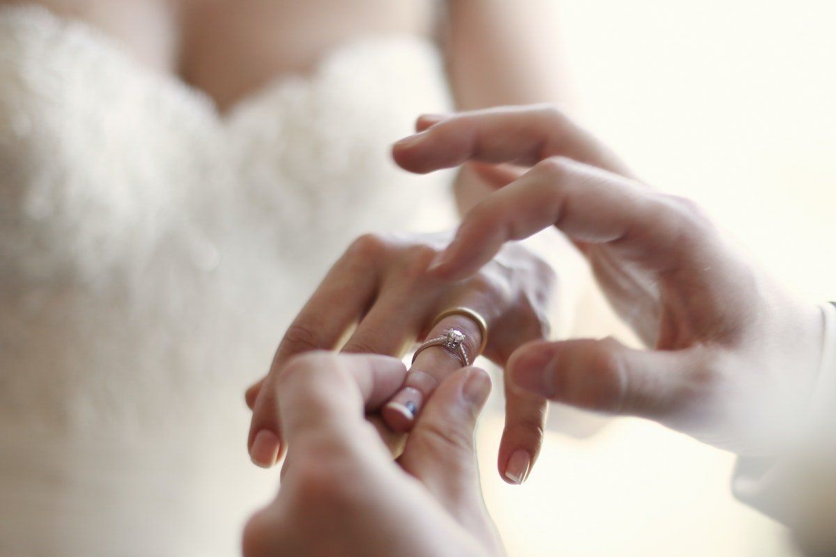 Hands placing a ring on a finger in a soft, bright close-up shot