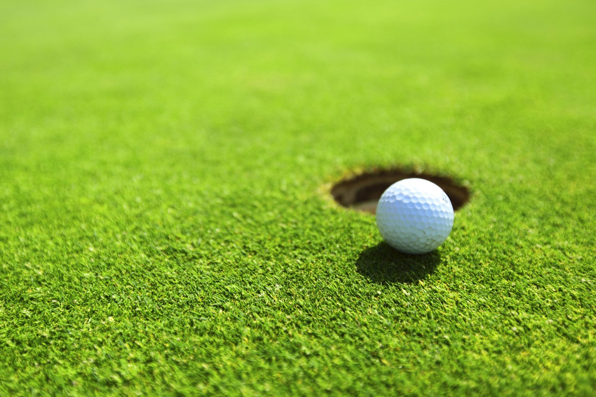 Golf ball beside the hole on a bright green putting green