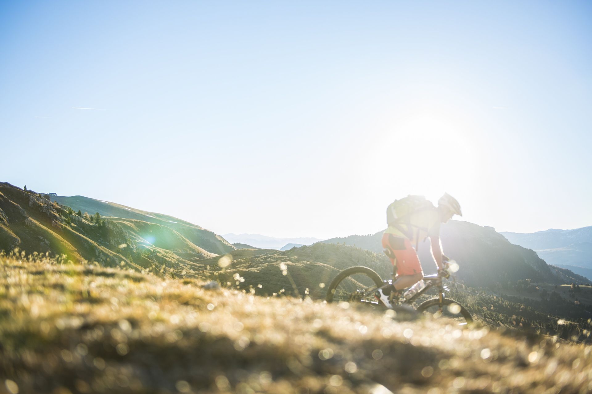 Cyclist riding on a sunlit mountain trail with bright lens flare and hills in the background