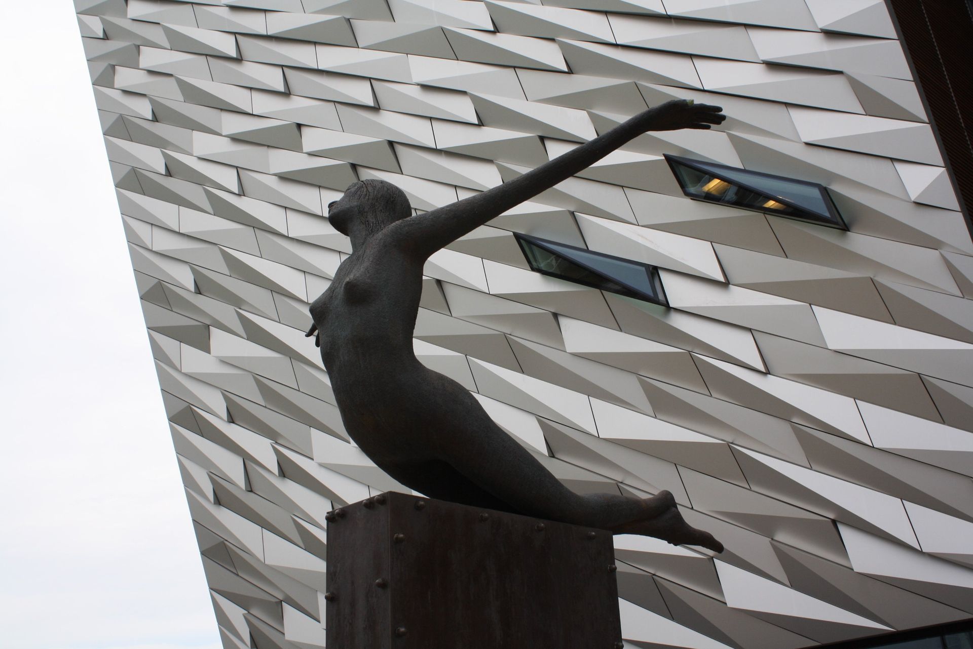 Dark abstract sculpture on a pedestal before a white geometric building facade