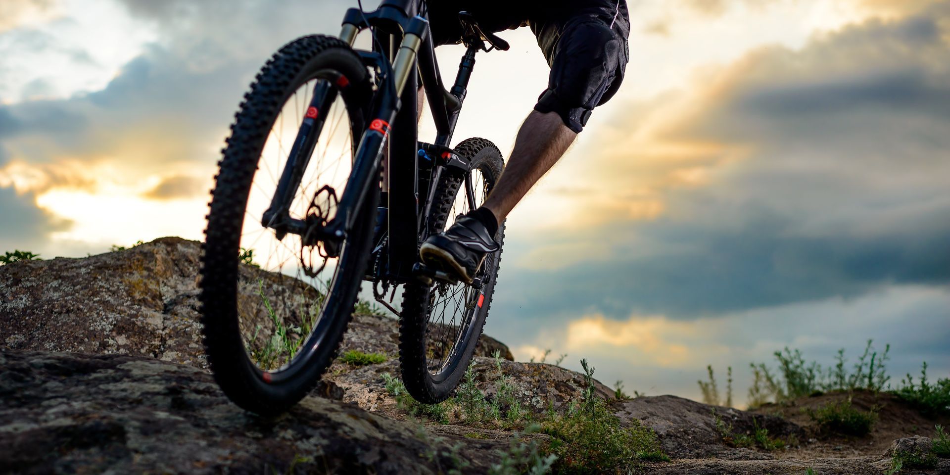 Mountain biker riding over a rocky trail at sunset, with a dramatic sky in the background