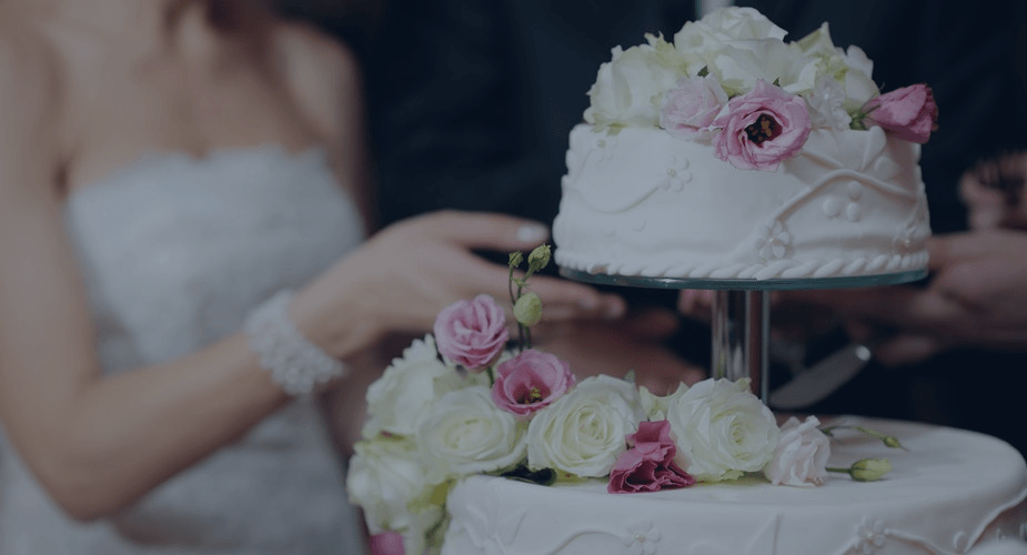 Wedding cake with white frosting and pink roses being decorated beside a bride in a strapless dress