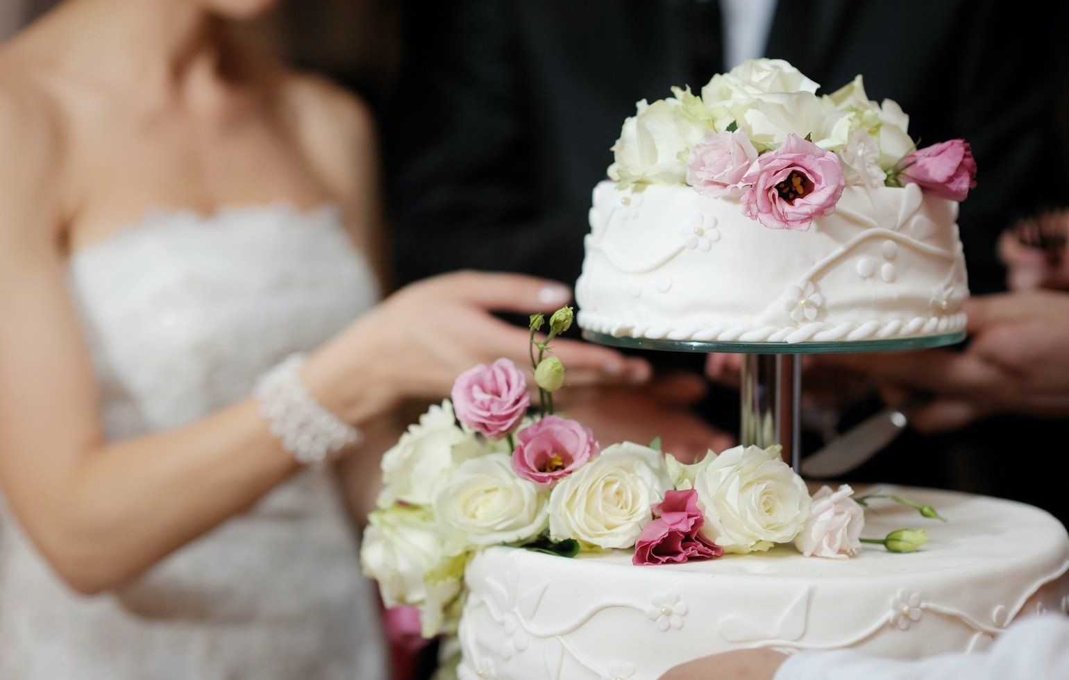 Bride placing a white tiered wedding cake decorated with pink and white roses