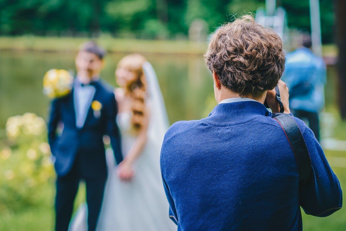 Wedding photographer taking a photo of a bride and groom outdoors in a green garden