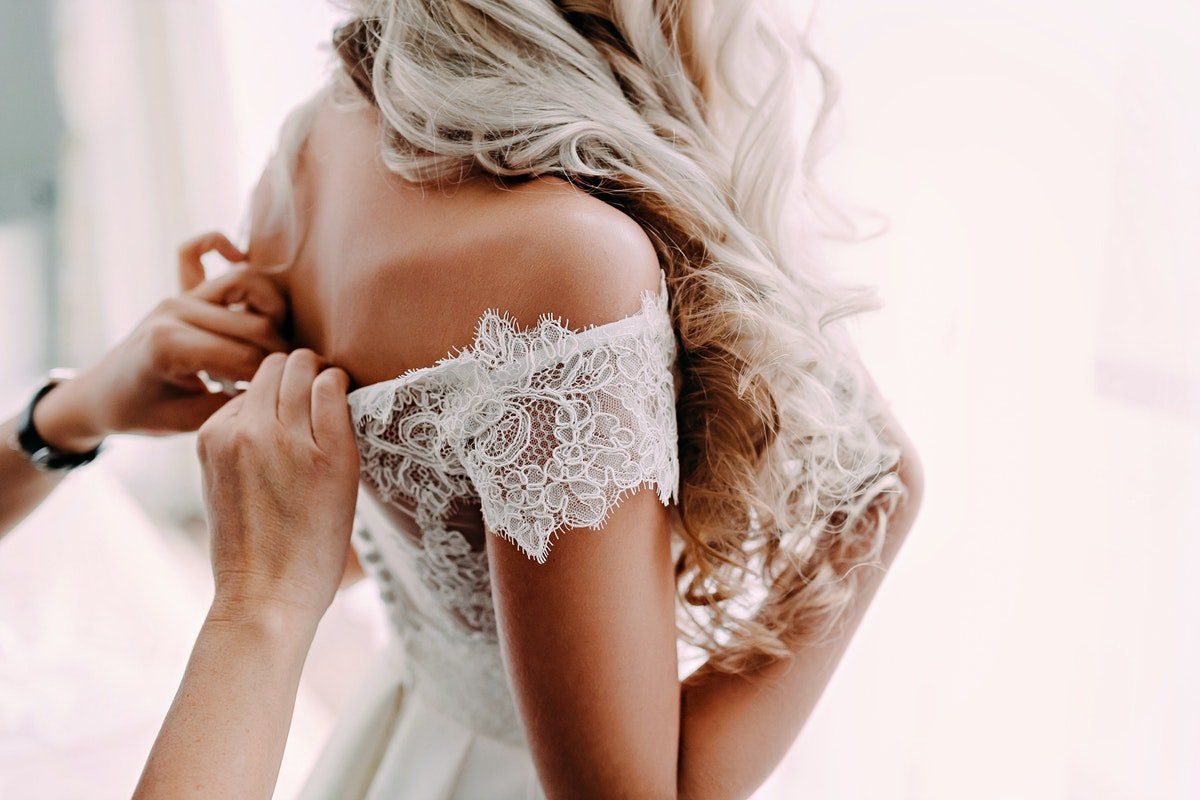 Woman adjusting a lace off-the-shoulder dress in a softly lit room