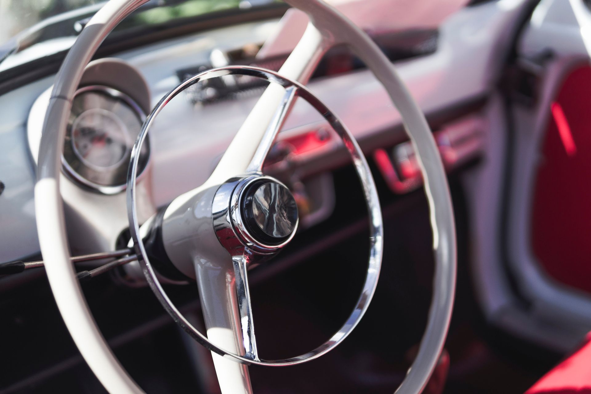 Close-up of a vintage car steering wheel and dashboard with chrome details and red interior accents