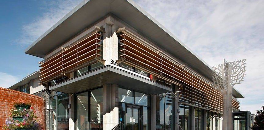 Modern building with glass walls, wood slats, and a sloped roof in an urban setting