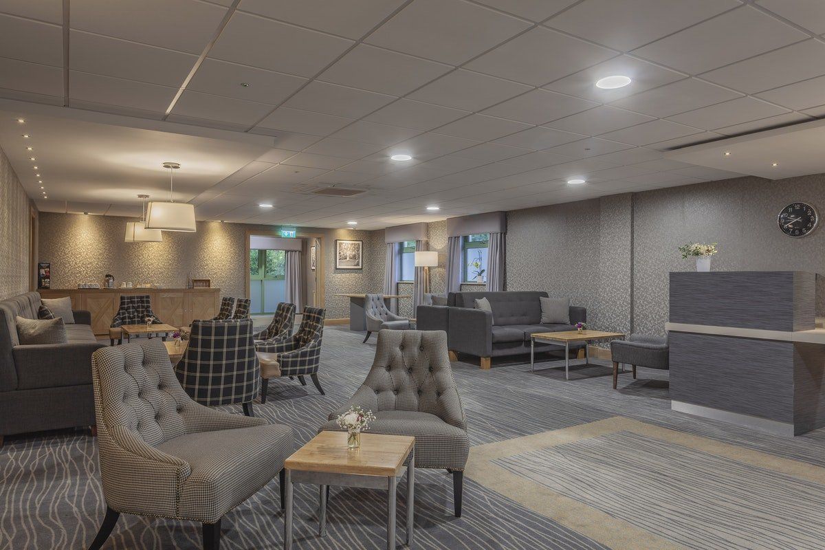 Spacious modern lobby with armchairs, sofas, tables, and a reception desk under recessed lighting.