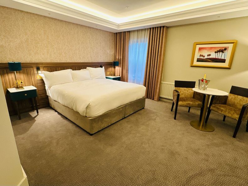 Hotel room with a neatly made bed, bedside tables, and a small desk by the window.