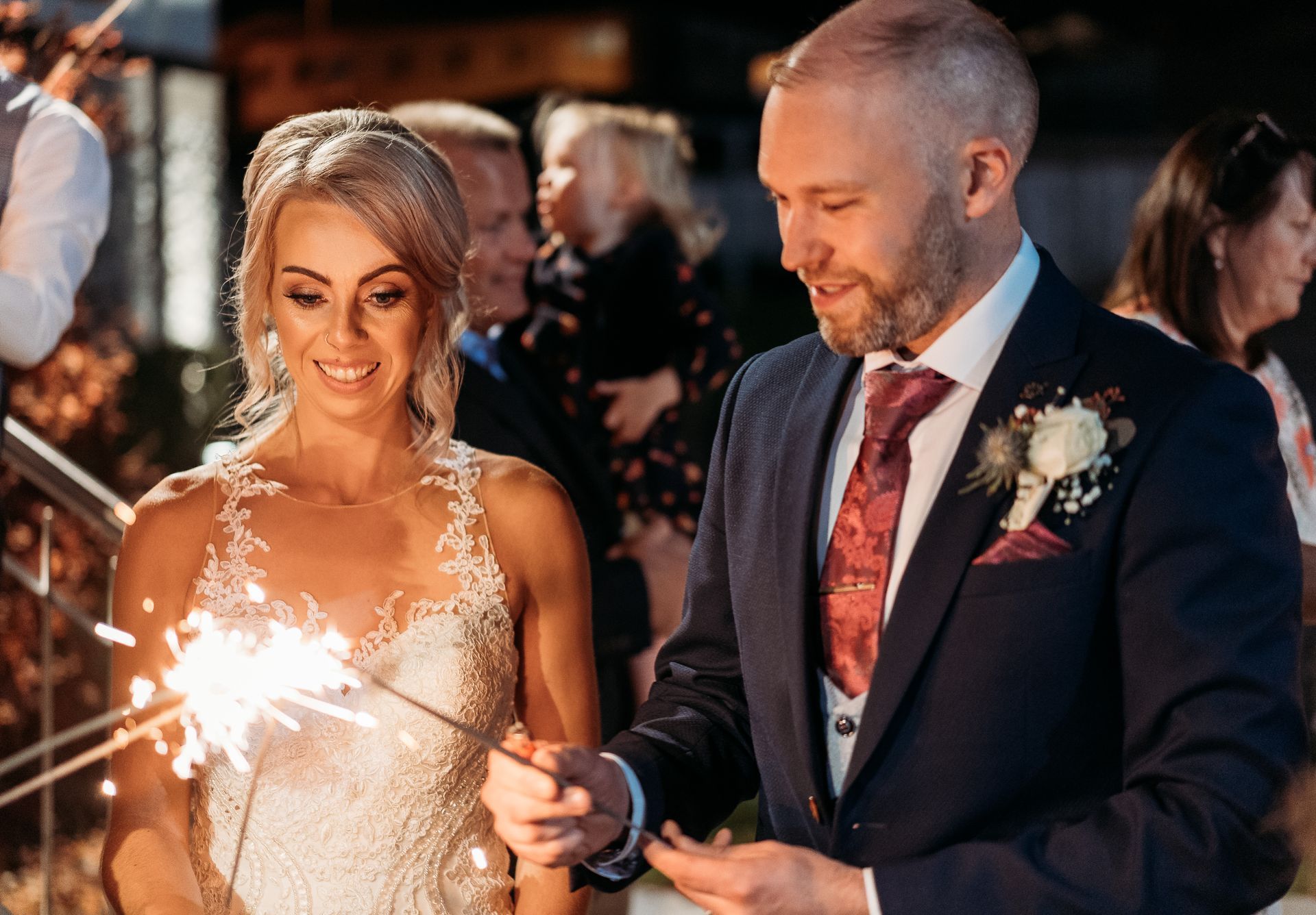 Bride and groom smiling while holding sparklers at an evening wedding reception