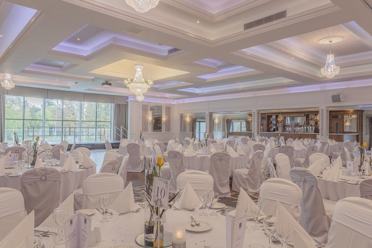 Elegant banquet hall with white table settings, chandeliers, and large windows overlooking greenery