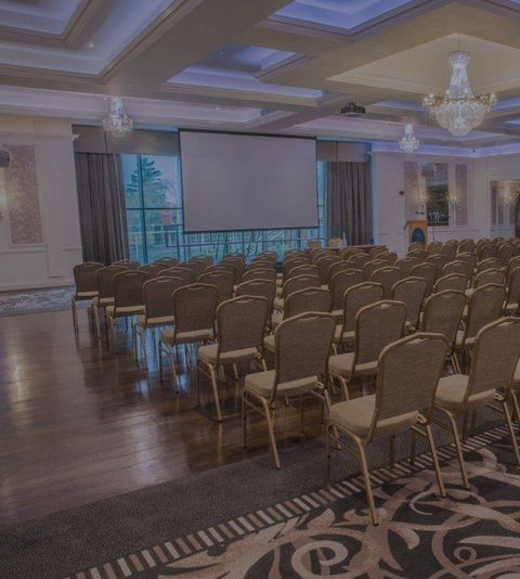 Empty conference room with rows of chairs facing a large projector screen and chandeliers overhead