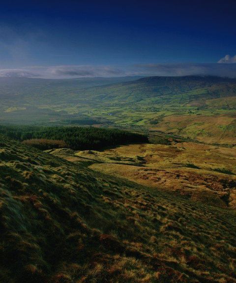 Rolling green hills and a wide valley under a blue sky with clouds