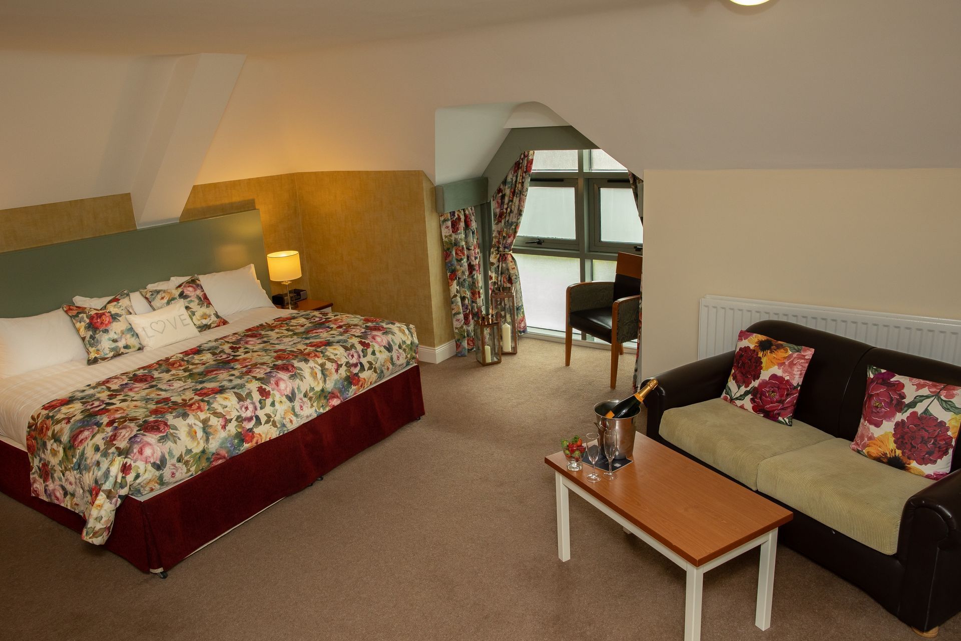 Cozy attic bedroom with floral bedspread, sofa, and small table under sloped ceiling