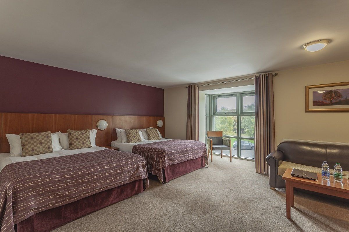 Hotel room with two double beds, balcony door, and seating area in neutral tones