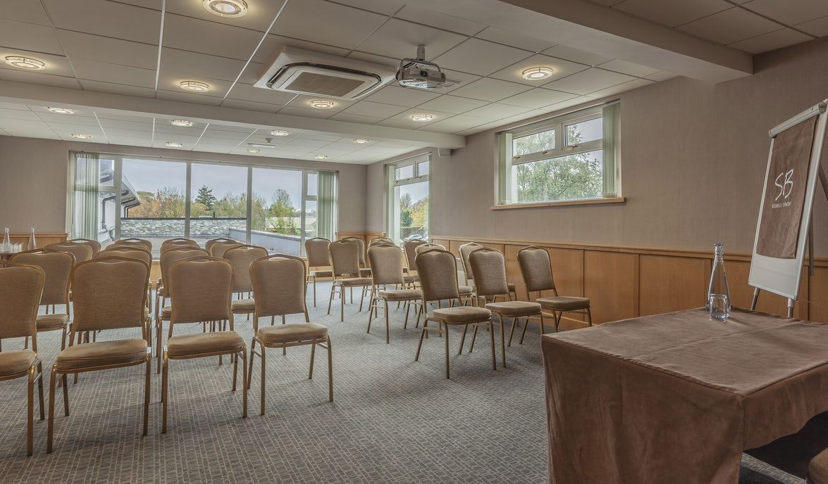 Empty conference room with rows of chairs, large windows, and a table at the front