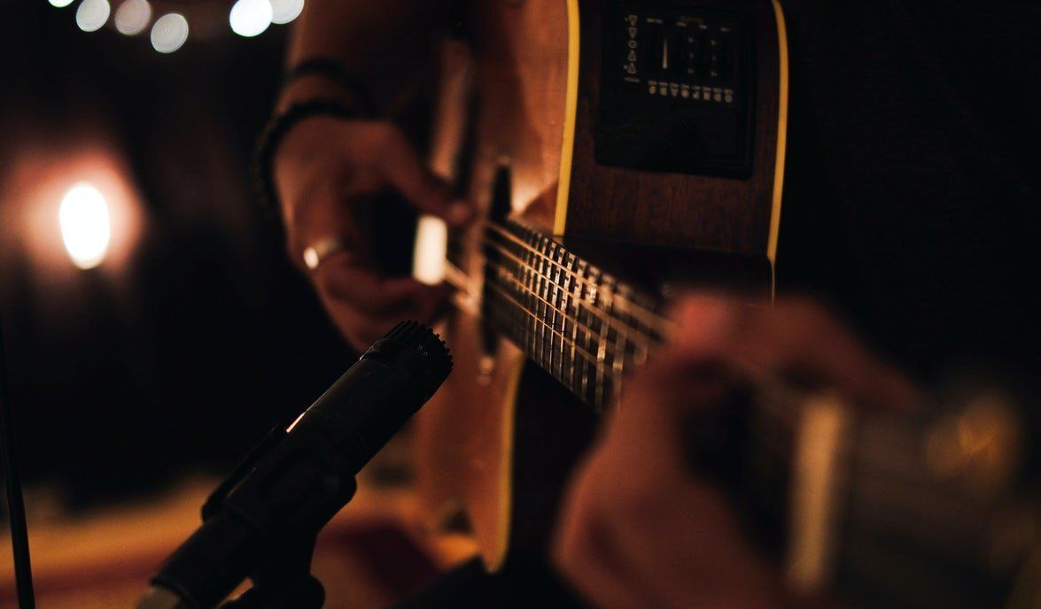 Close-up of hands playing an acoustic guitar in warm, dim light with a microphone nearby