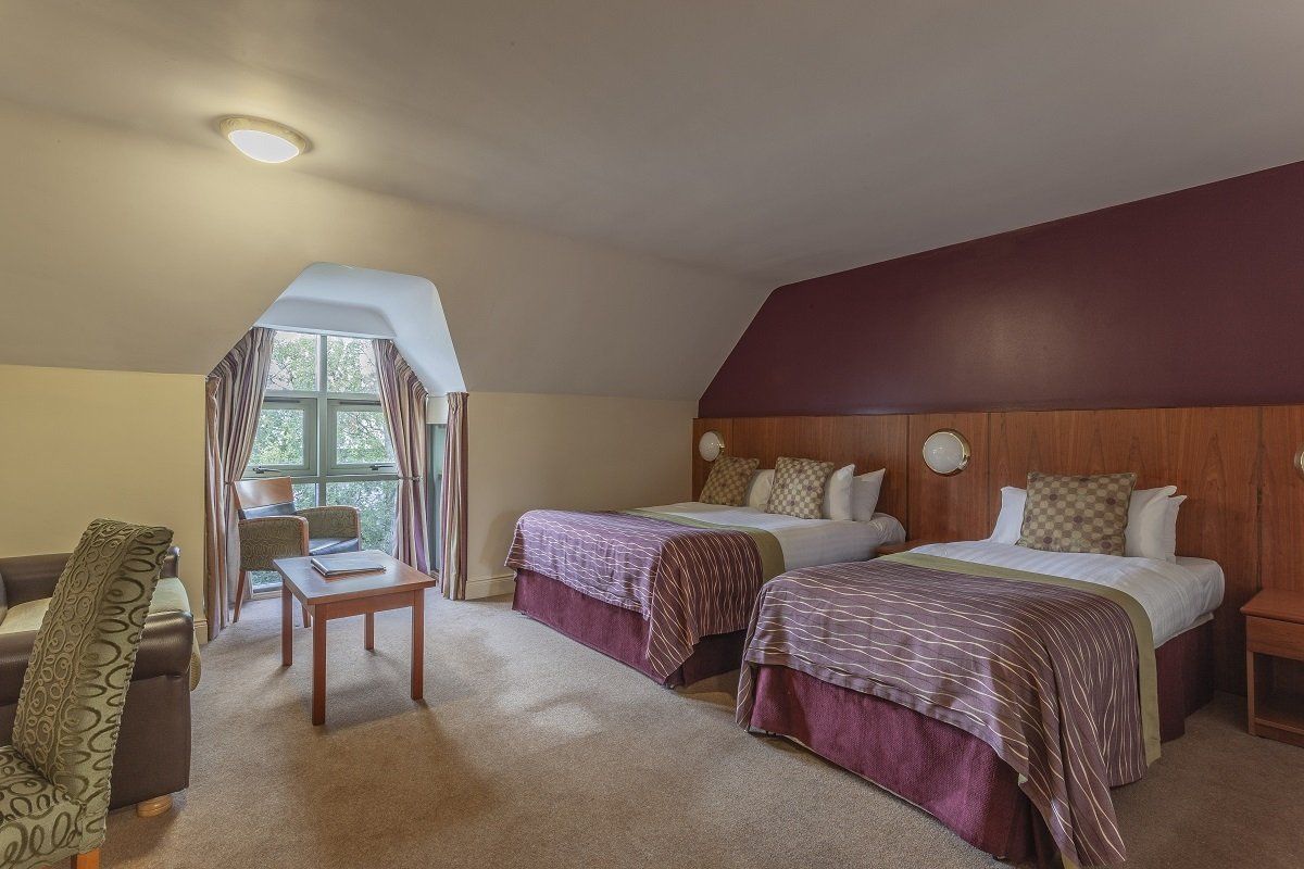 Hotel room with two queen beds, mauve decor, and a window seating area.