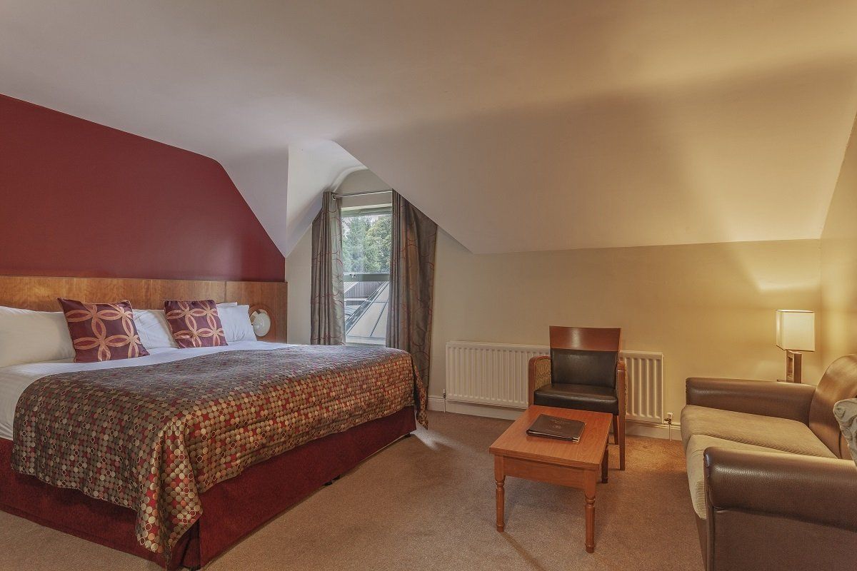 Cozy attic bedroom with a double bed, sofa, coffee table, and window seat under a sloped ceiling