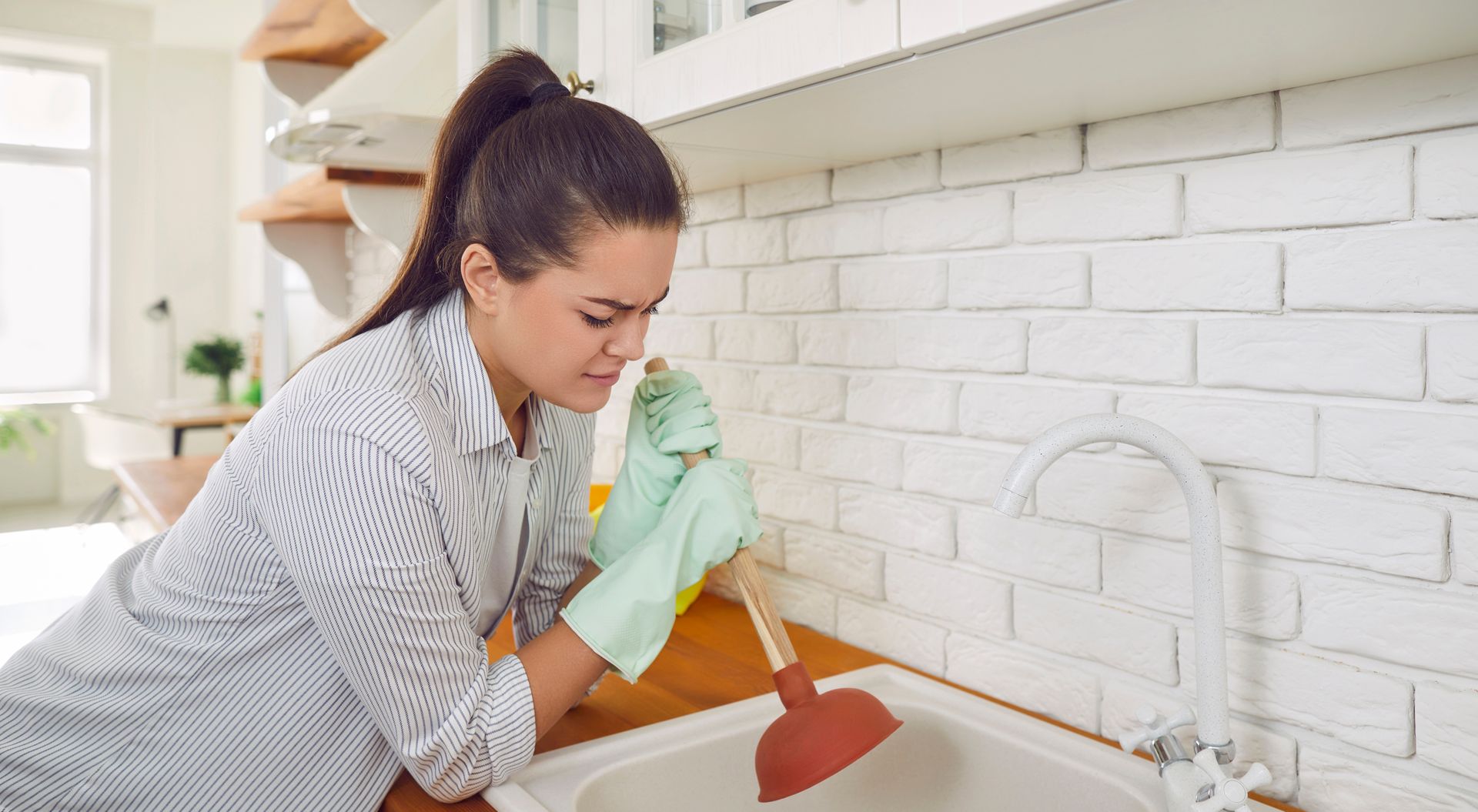 Woman using a plunger trying to unclog a kitchen sink drain