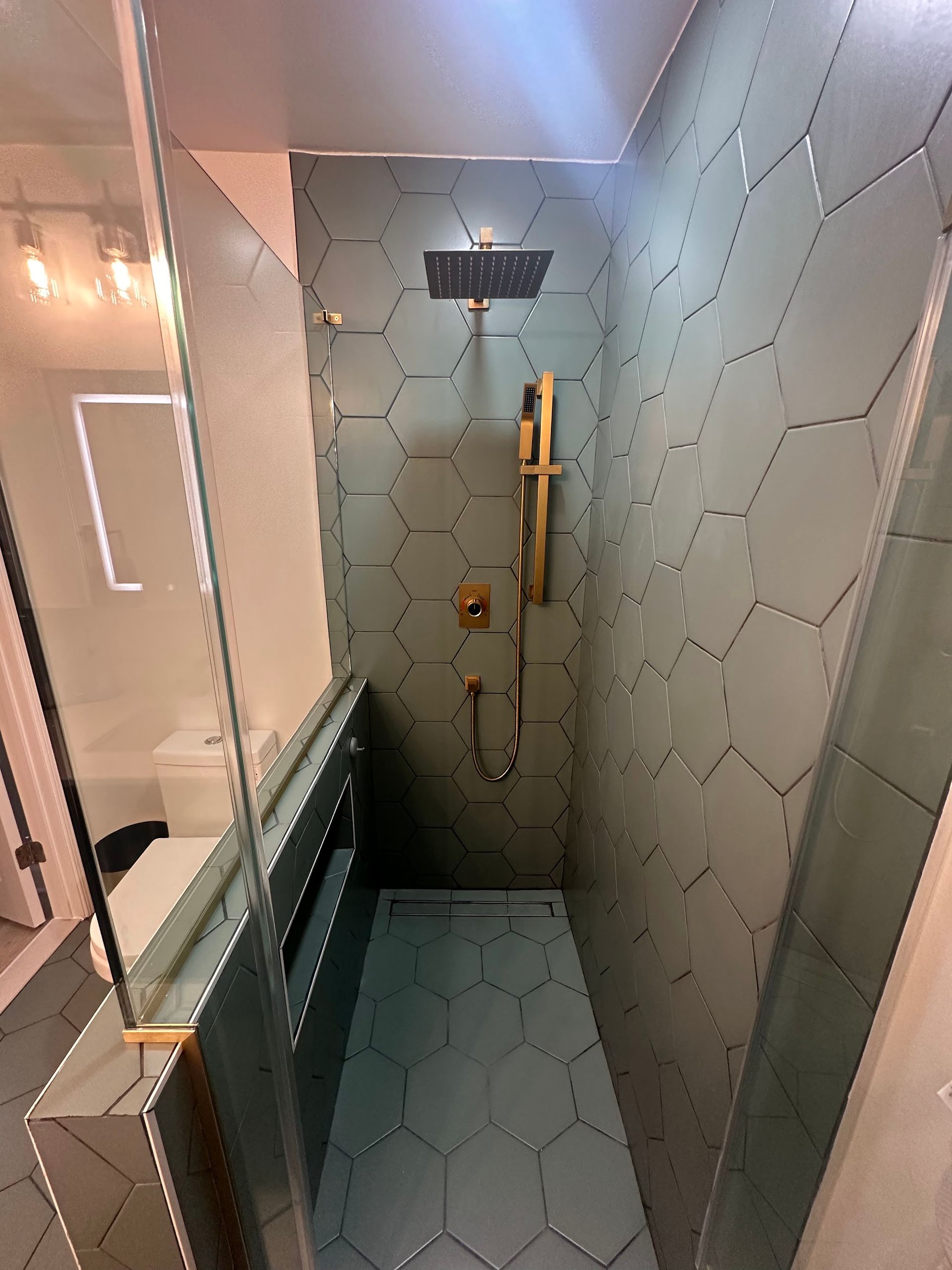 Green tile shower in Baltimore City with half wall, frameless custom glass, handheld fixture, and 8-inch hexagon tile on walls and floor