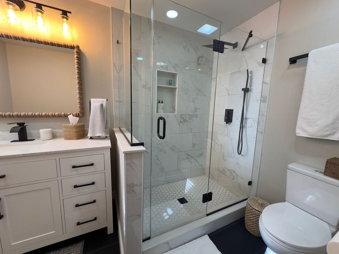 Modern bathroom in Finksburg with black-tiled walk-in shower featuring a half-wall and frameless glass, black fixtures, and double vanity