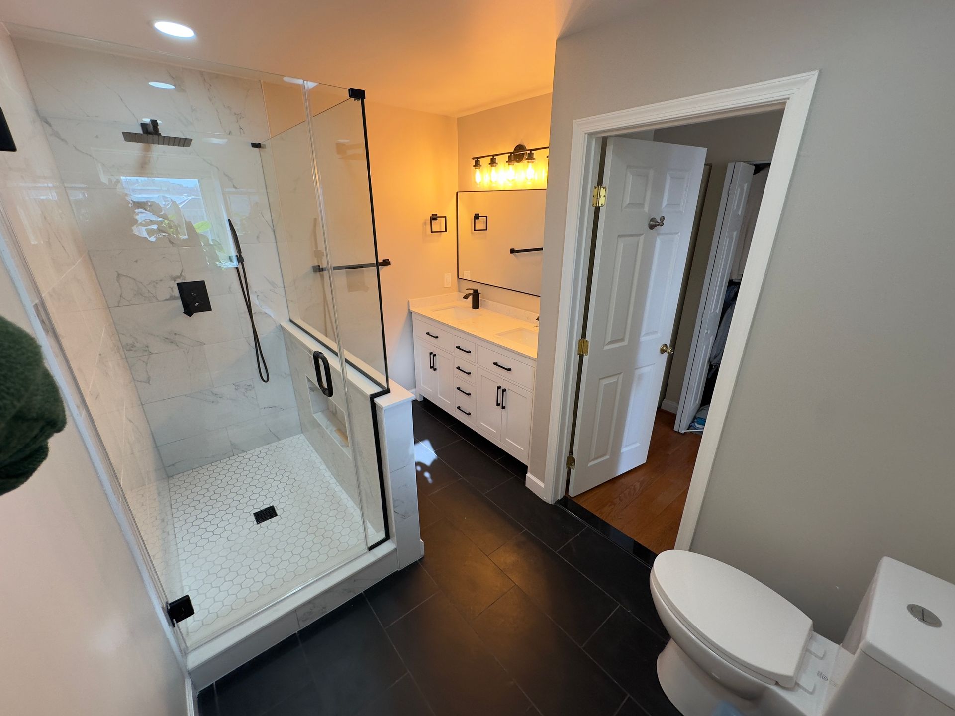 Modern bathroom in Finksburg with frameless glass door, black fixtures, white wall tile, black floor tile, built-in niche, and unique mirror