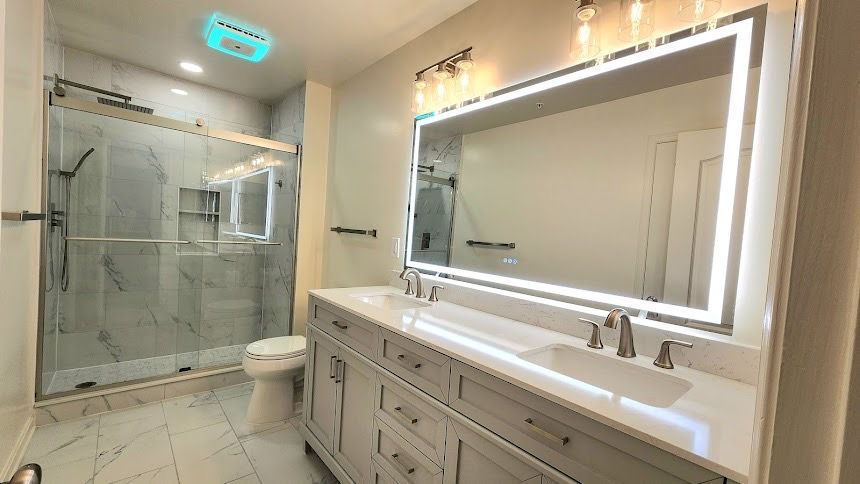 Bathroom remodel in Finksburg with double vanity, LED mirror, walk-in shower with marble-look tile, frameless glass door, and Bluetooth exhaust fan