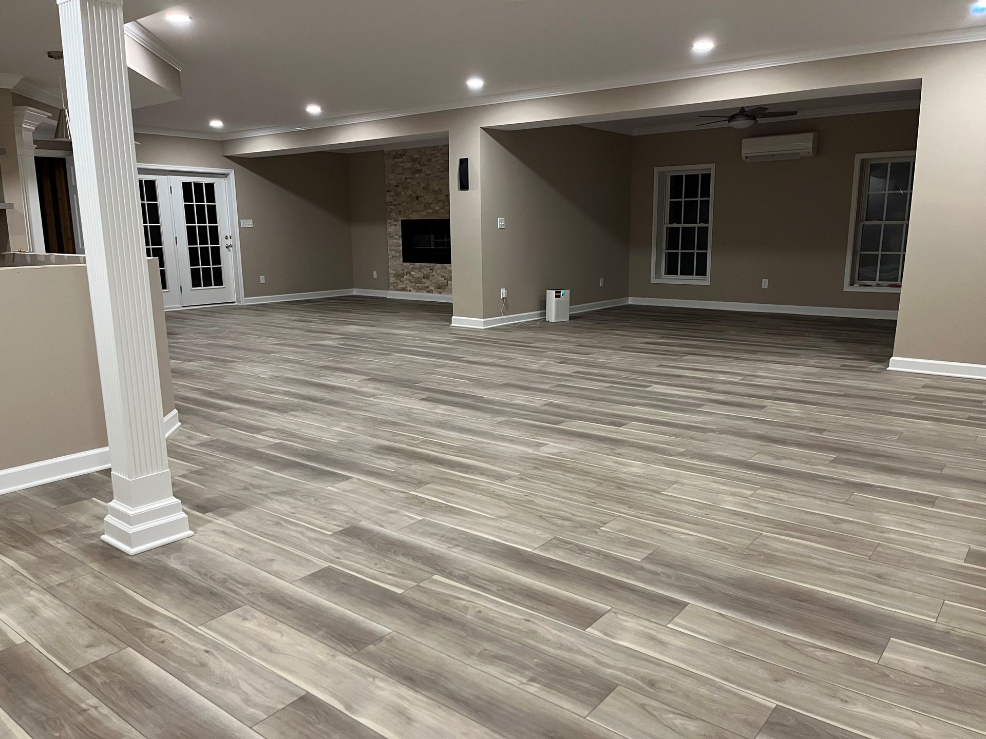 Finished basement in Finksburg with LVP flooring, U-shaped wet bar, stacked stone fireplace, French glass doors, bedroom, gym, and bathroom